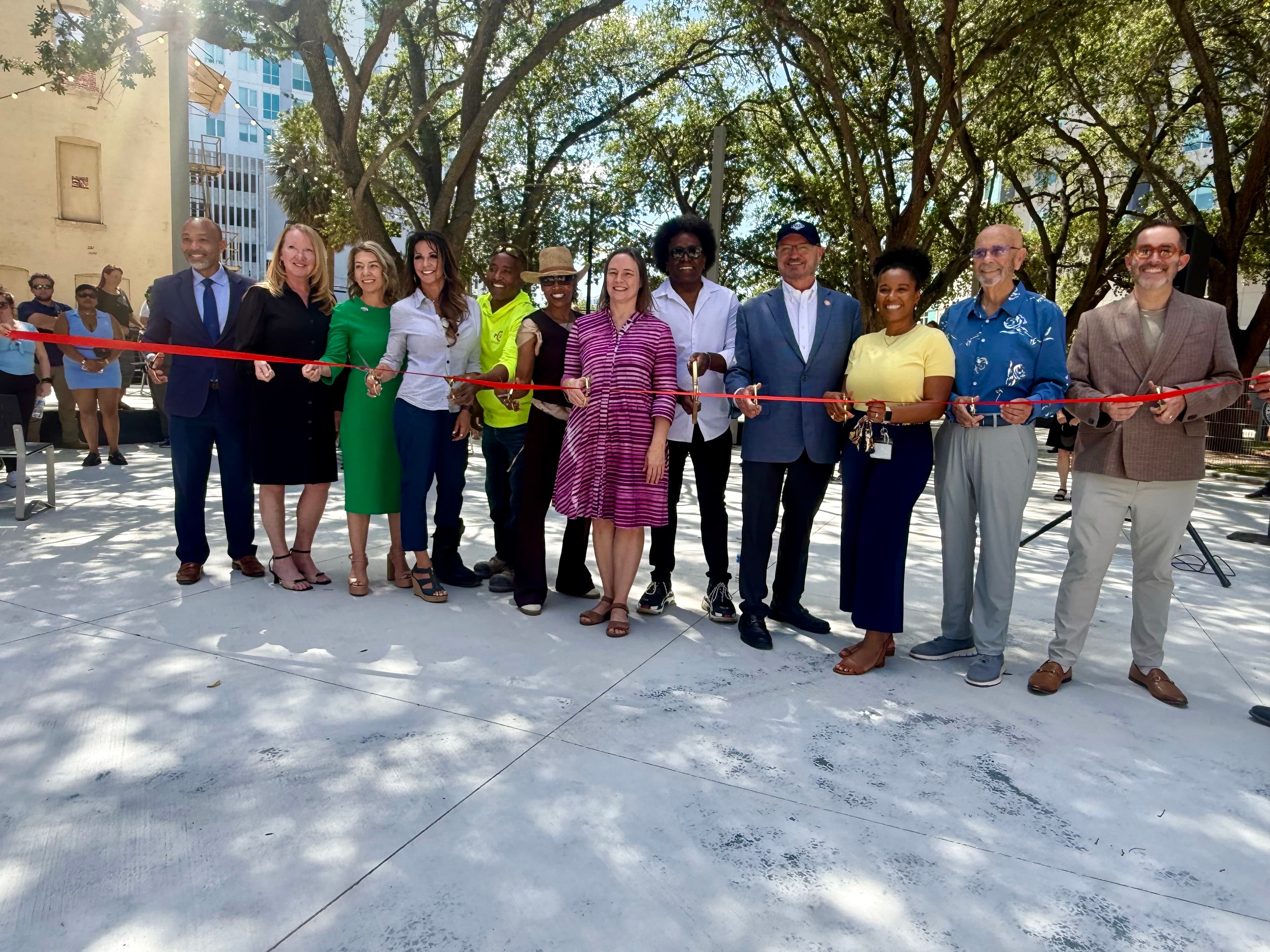 12 people holding gold scissors about to cut a red ribbon to celebrate park opening