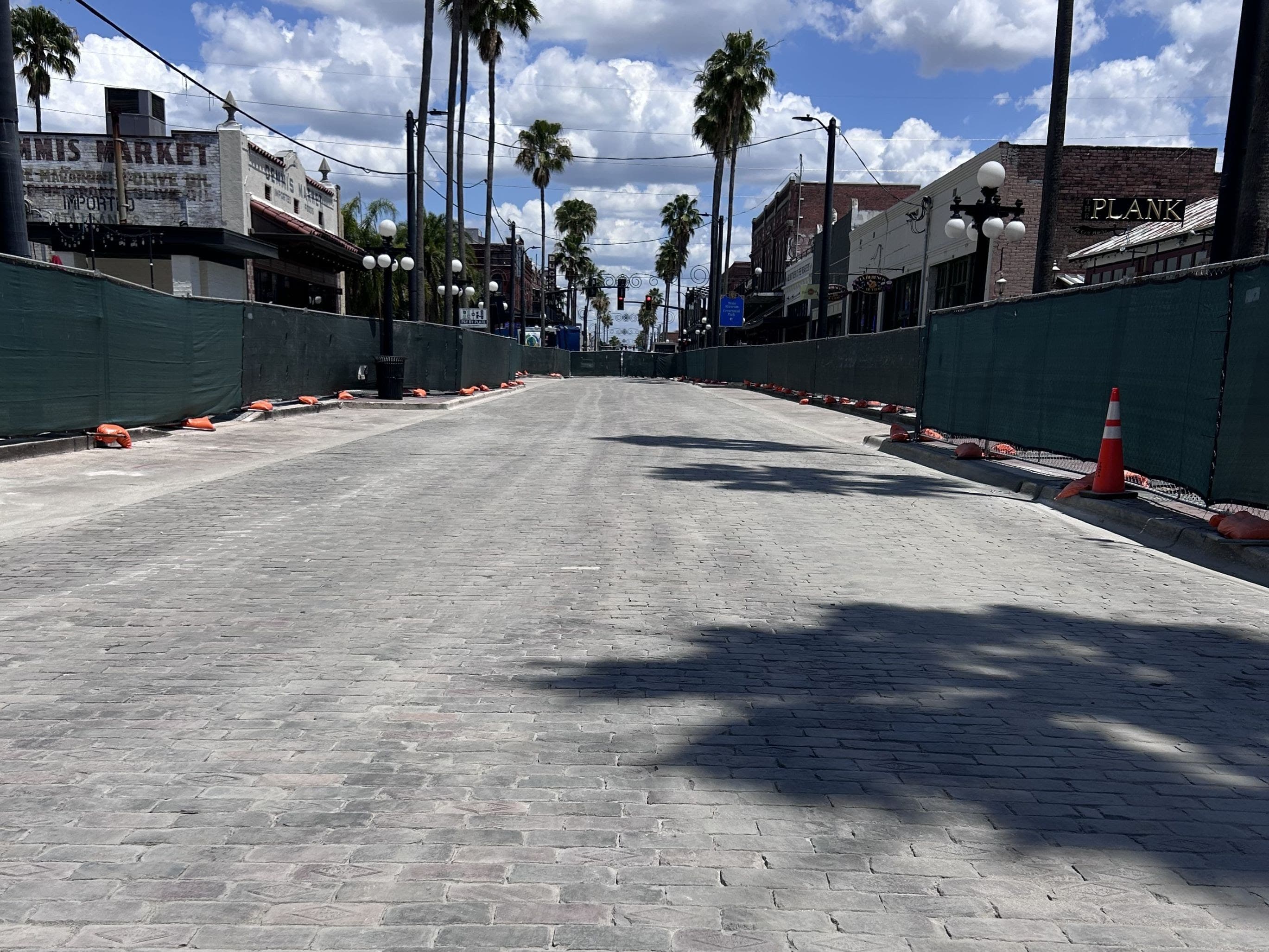 Grey historic bricks down a street with green construction fences on each side.