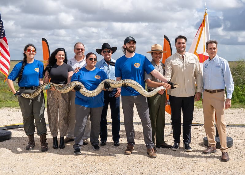 10 people smiling with a large python spread out between 6 of them