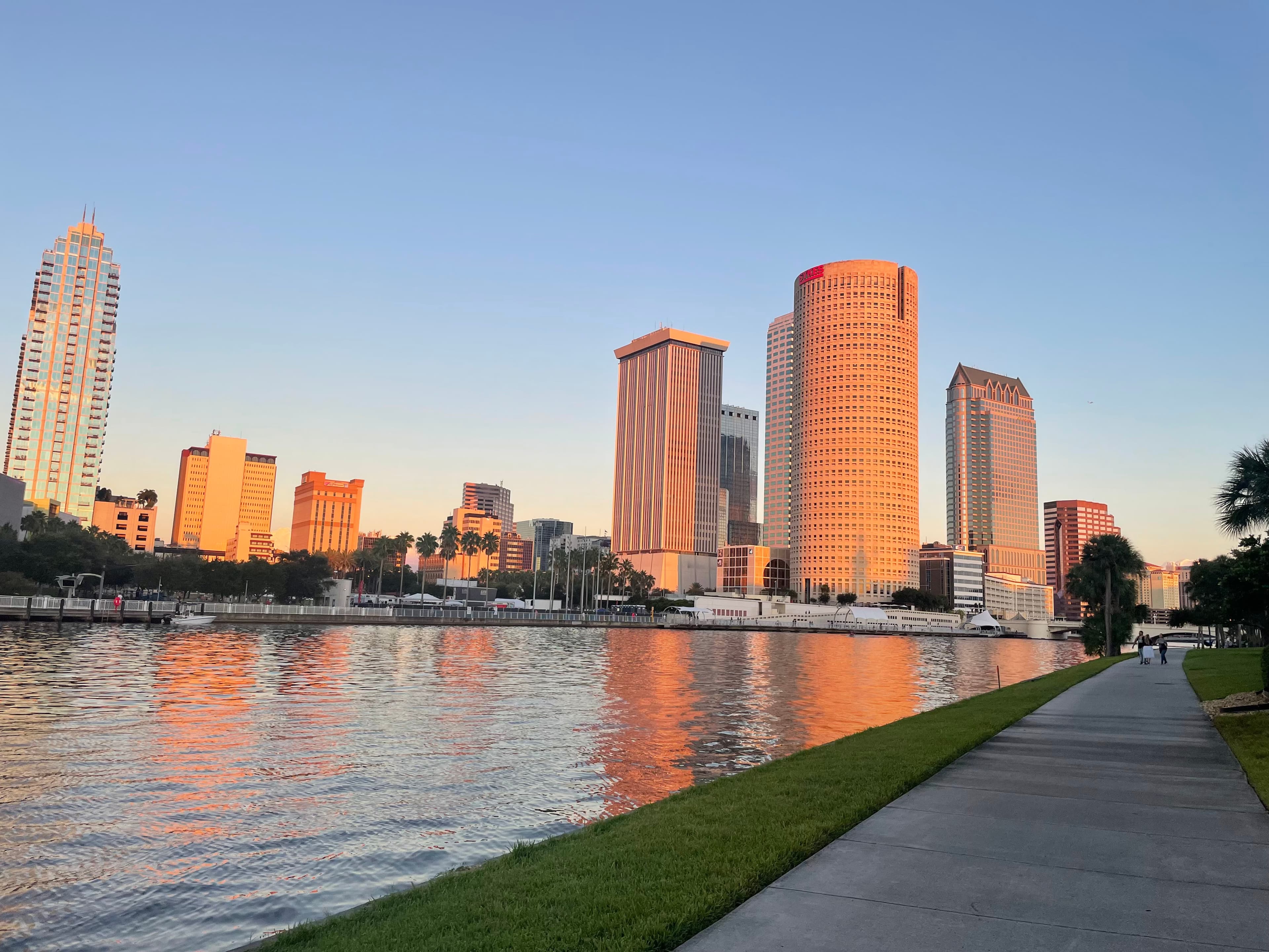 Sidewalk in front of a river with large city buildings in the background.