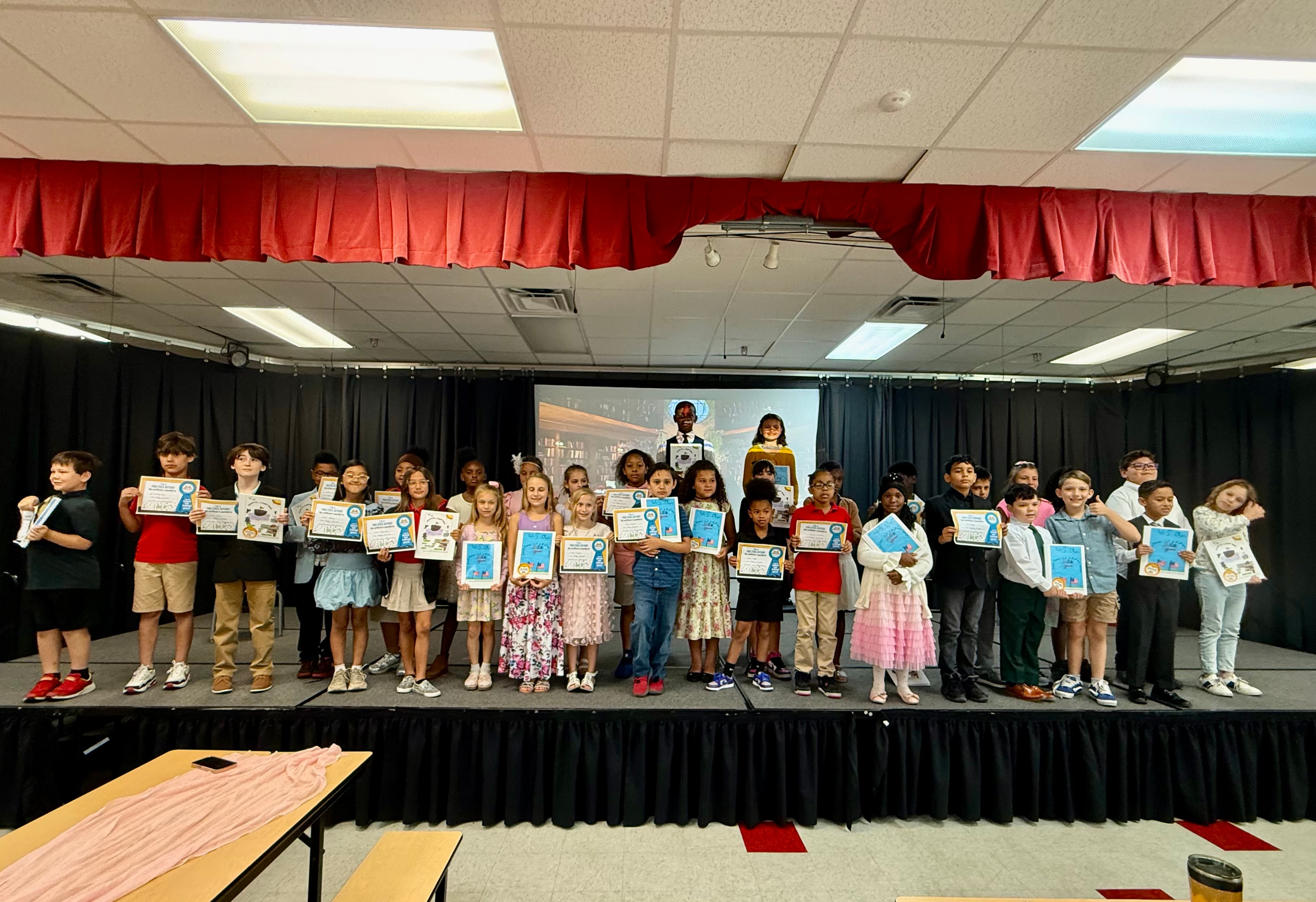 33 students standing on stage with books smiling at the camera