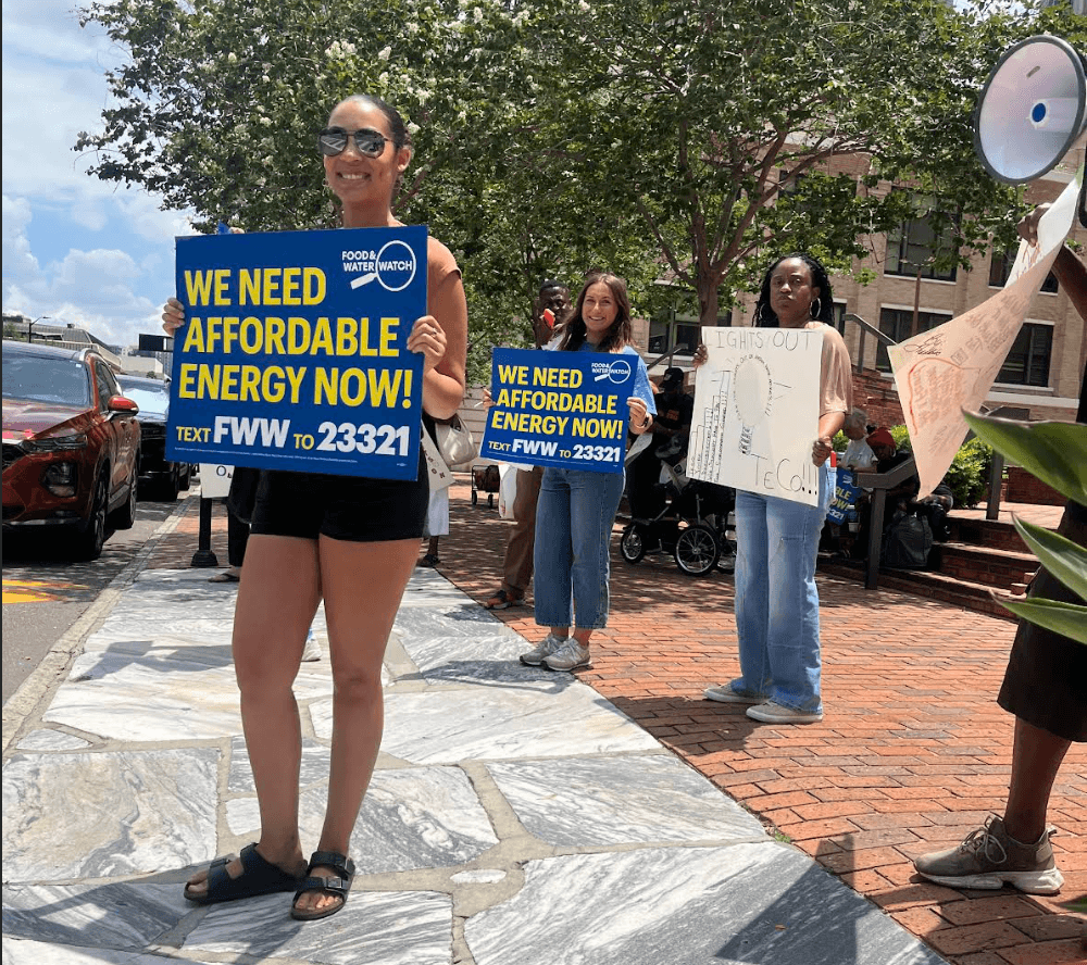 Three ladies holding blue sigs that say we need affordable energy now in yellow.