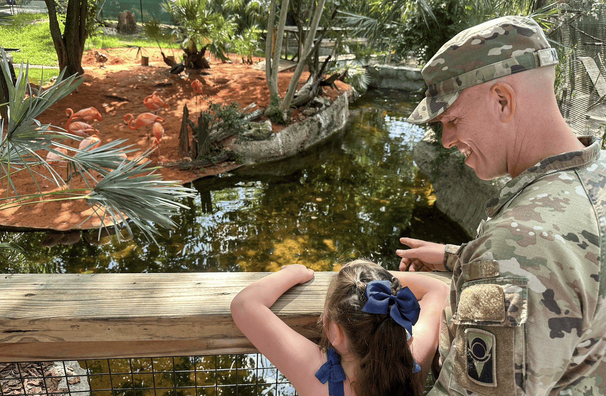 a young girl and a active service member looking at flamingos