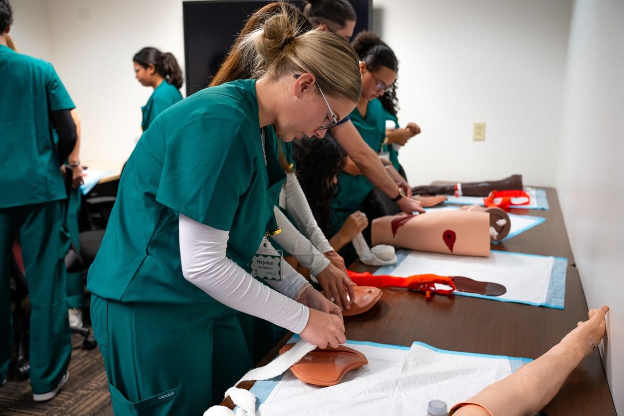 students in teal scrubs working on fake bodies