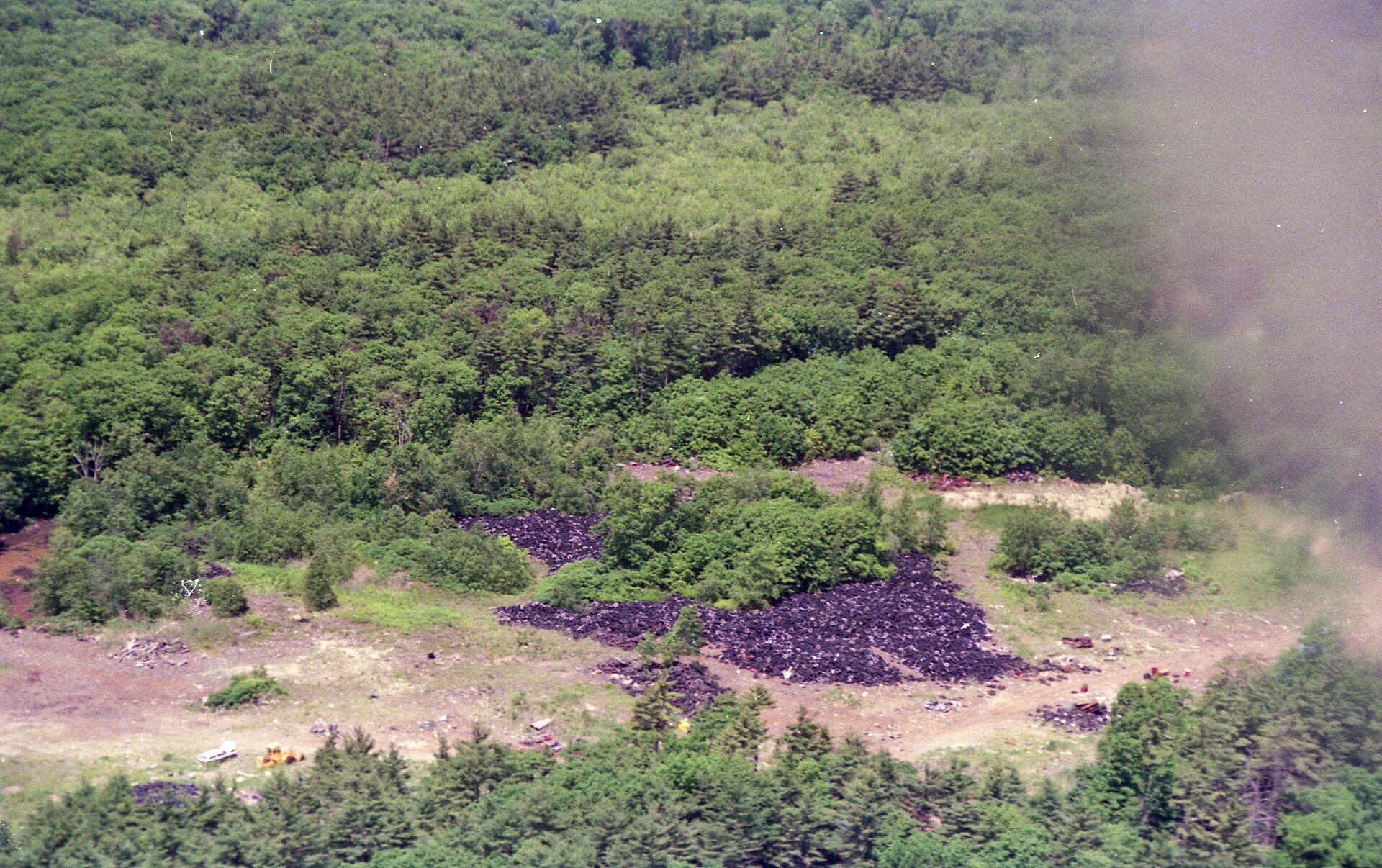 Aerial view of large piles of discarded tires in a forest clearing