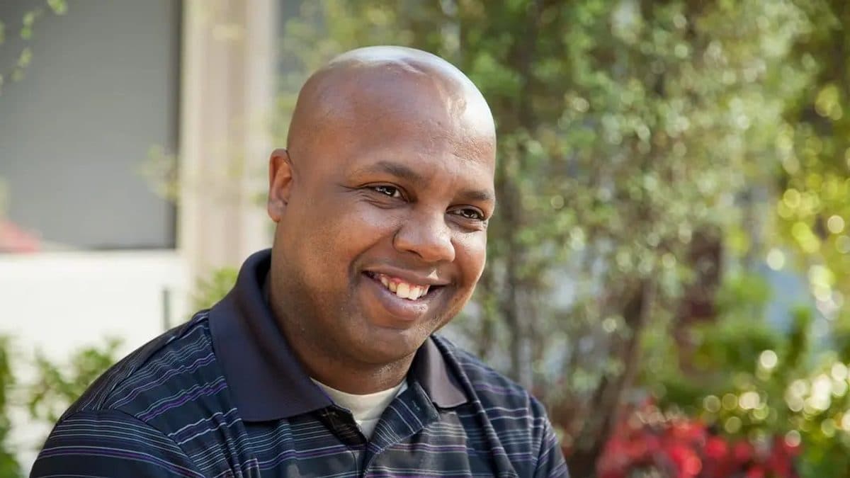 A person wearing a Frazier Brand t-shirt with Courage is Contagious printed on it, standing in a simple setting.