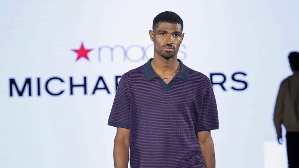 Isiah Thornton, male model, stands in a studio or runway setting, wearing a styled outfit, facing the camera.