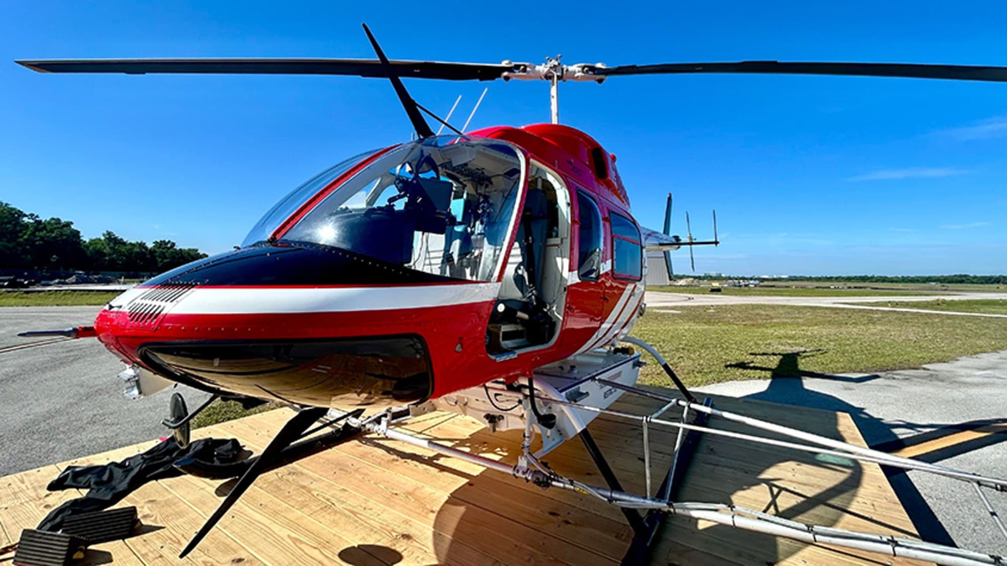 Red and white Hillsborough County Mosquito Management helicopter with spray booms parked on a wooden pad at an airfield